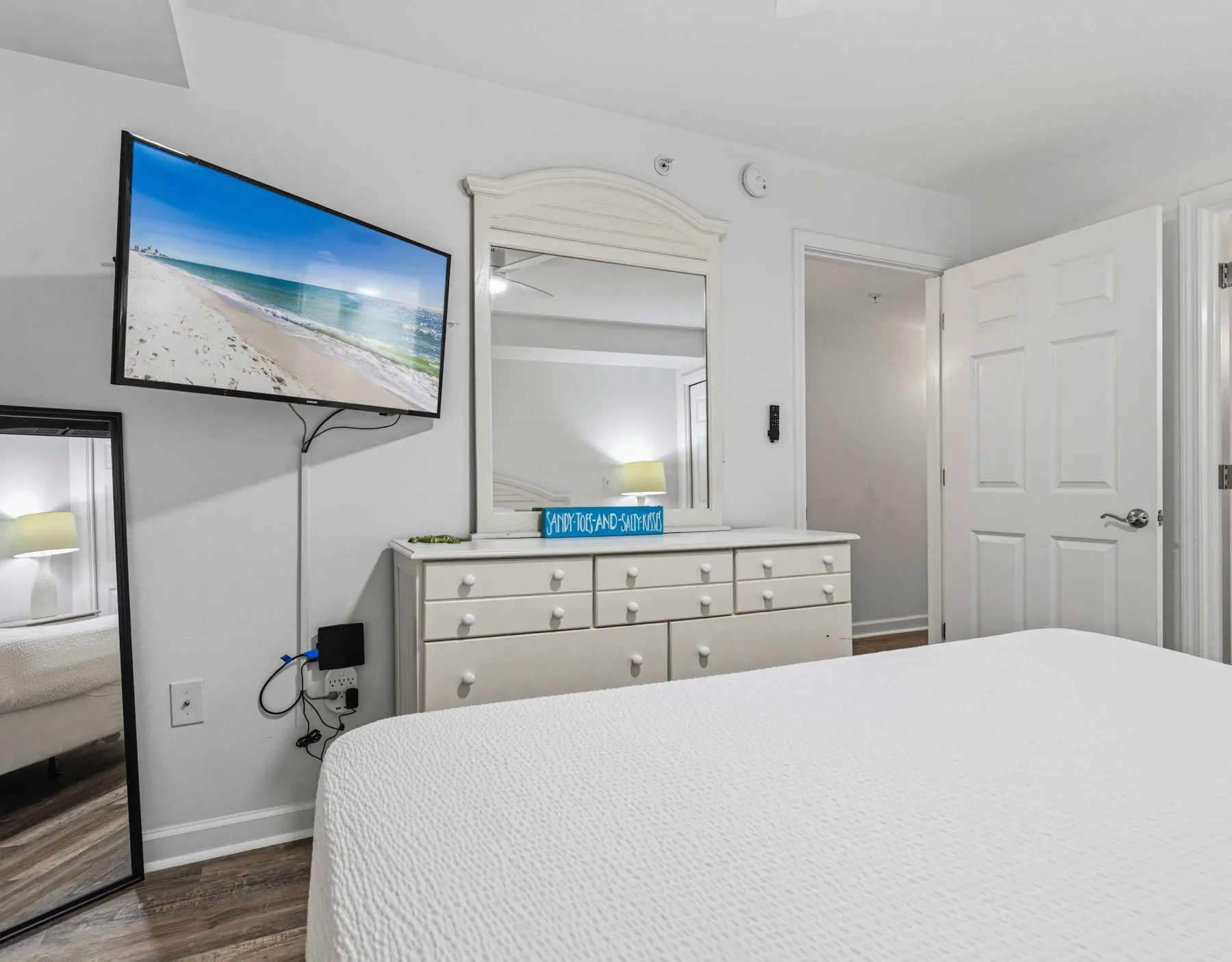 Un dormitorio con cama, cómoda, espejo y televisor montado en la pared.