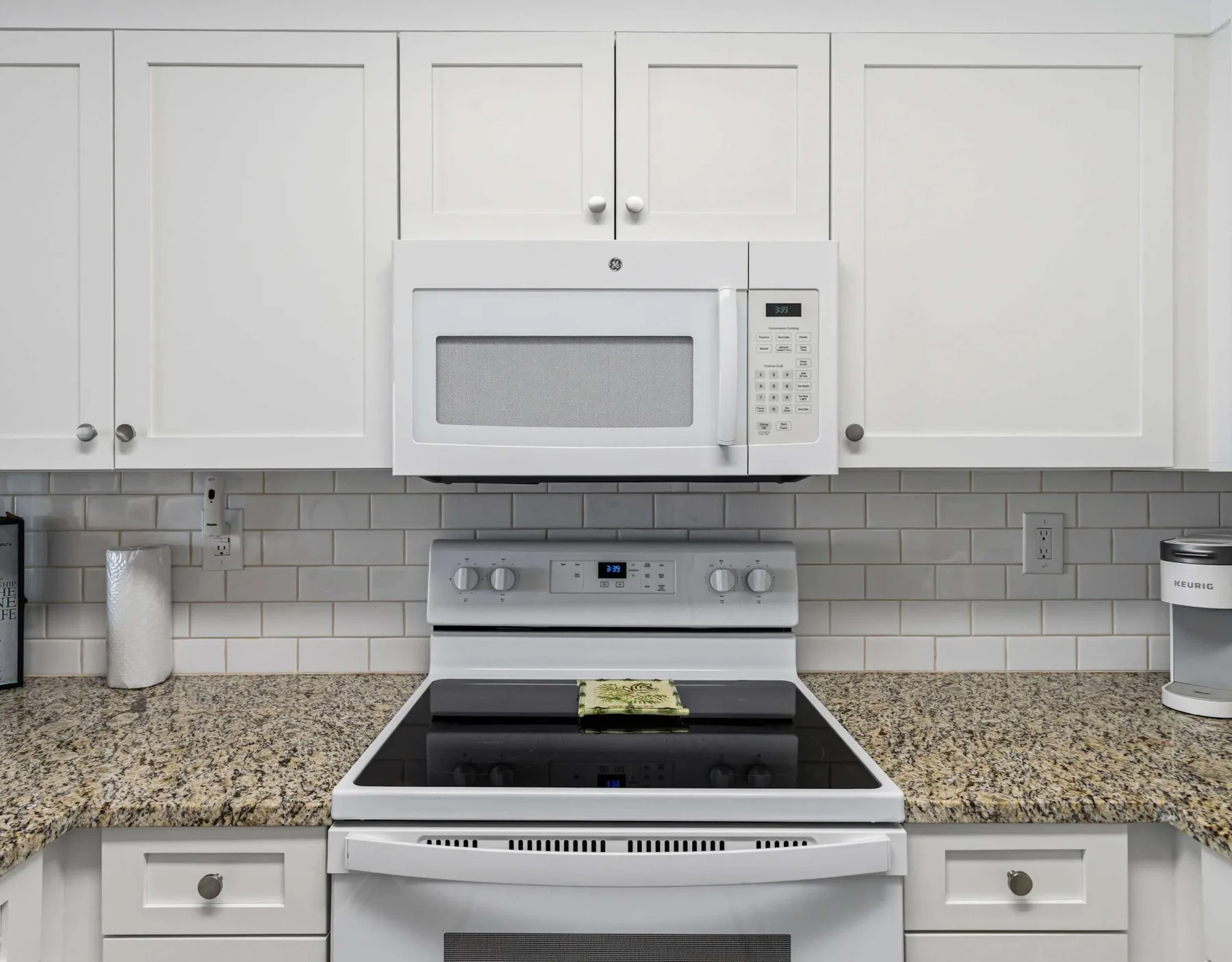 Una cocina con gabinetes blancos, una estufa y un microondas.