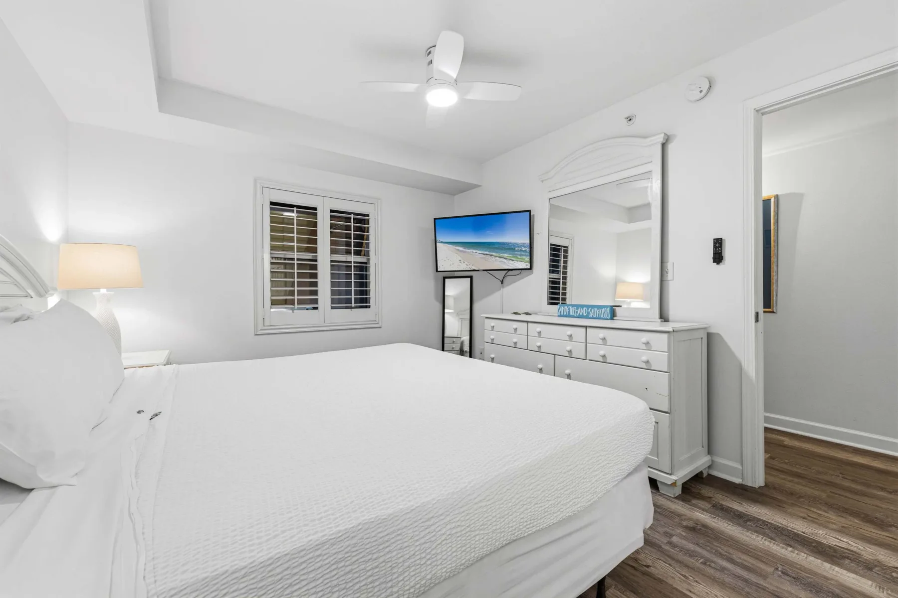 Un dormitorio luminoso con una cama grande, una cómoda y un televisor en la pared.