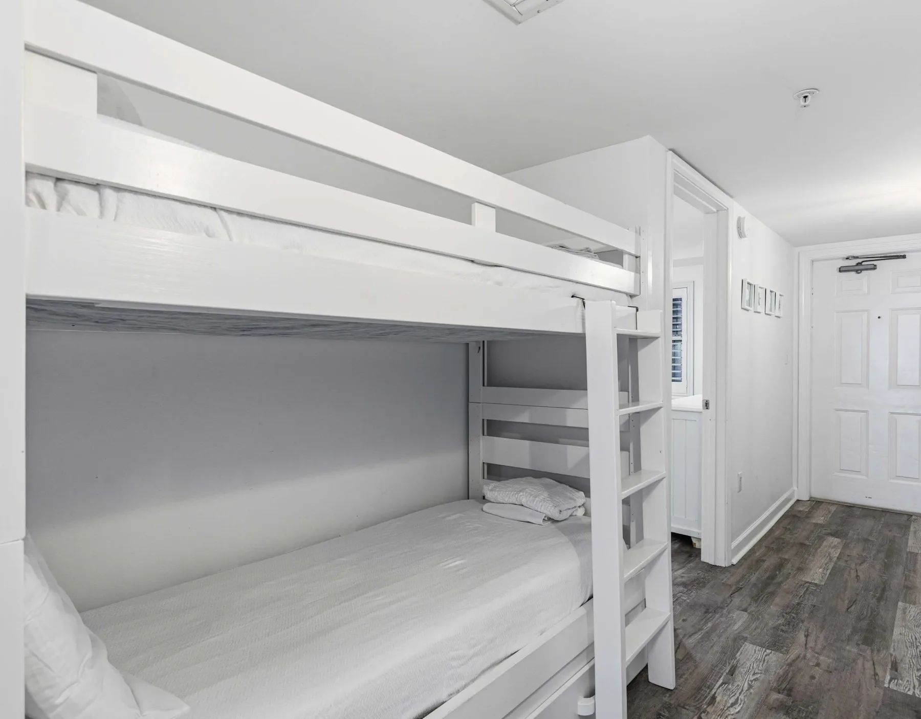 Un dormitorio con literas blancas y suelo de madera oscura.