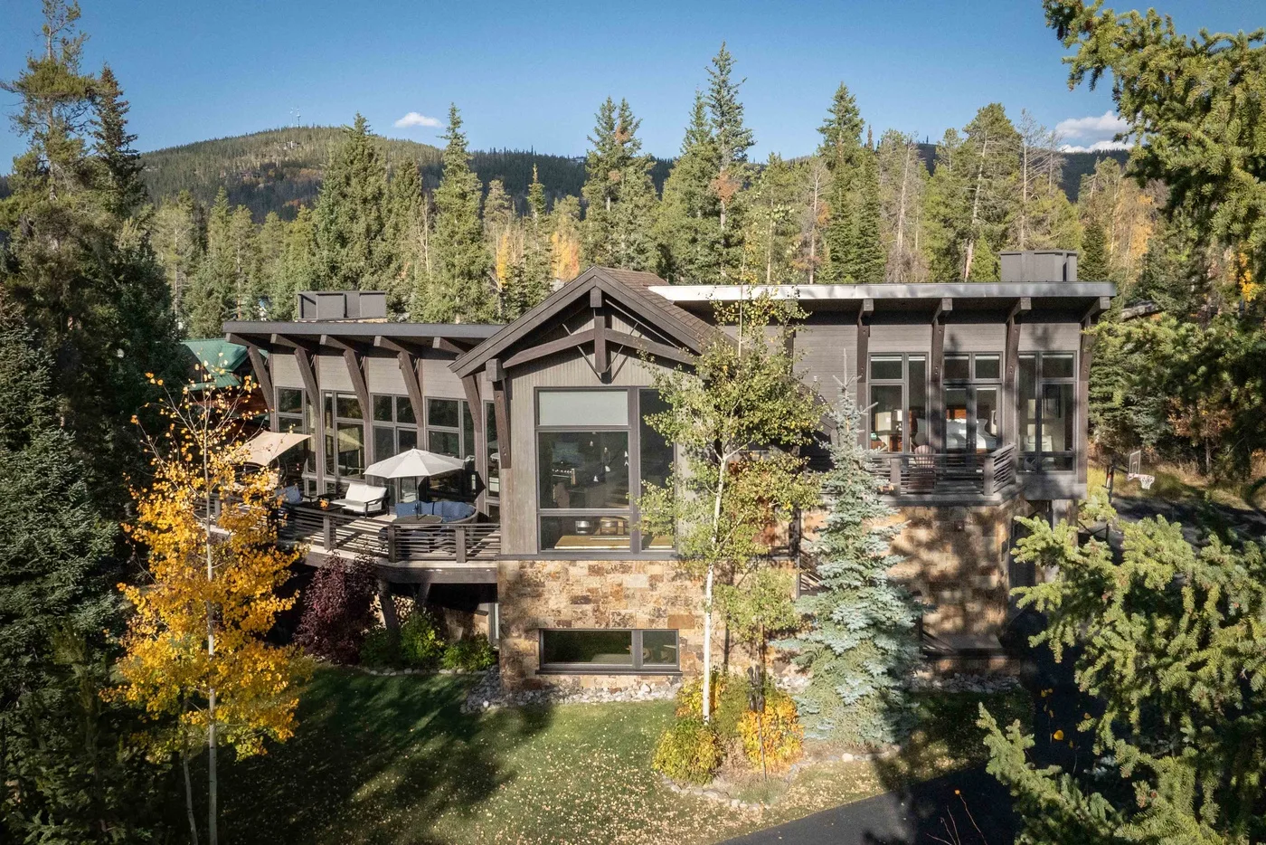 A modern mountain house sits among trees, with forested hills in the background.