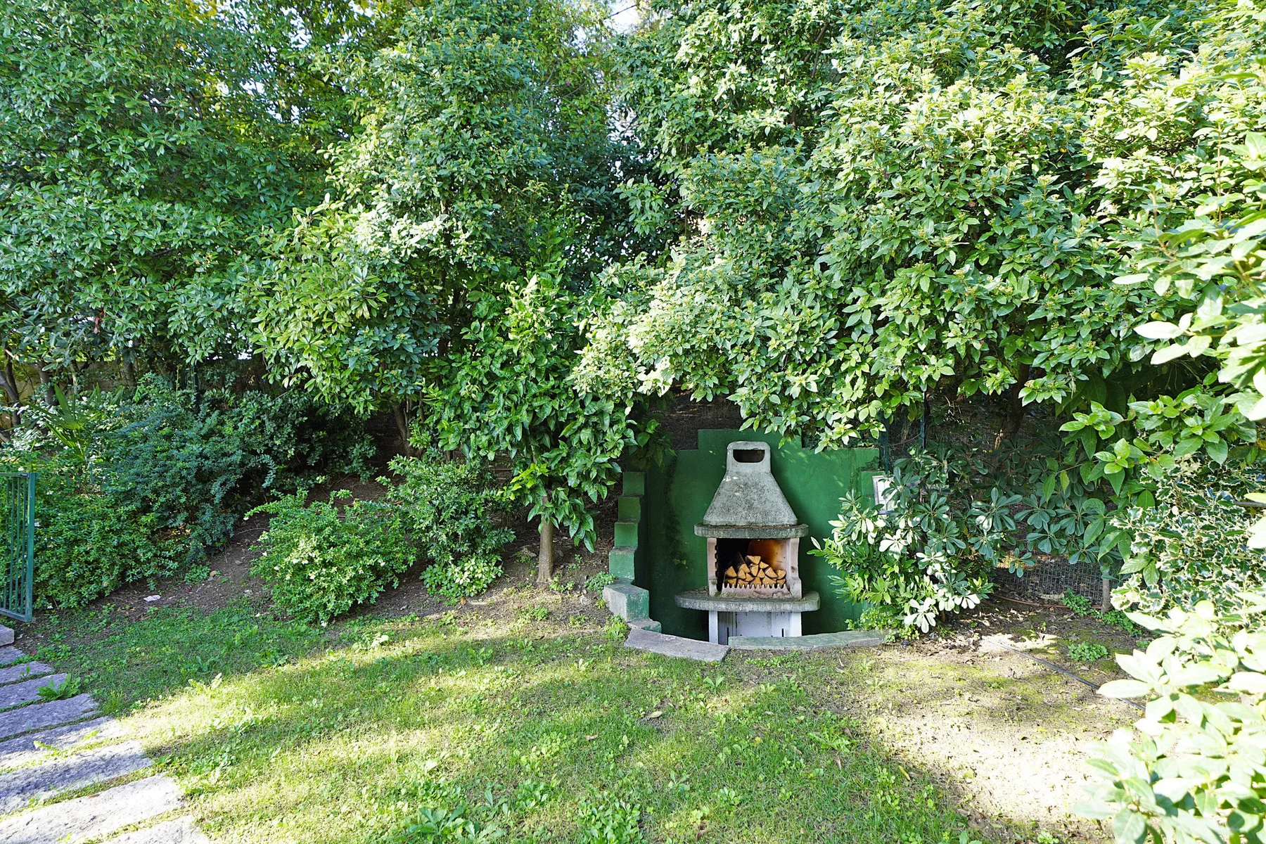 Zona común: Una zona de jardín con una chimenea exterior entre árboles frondosos.