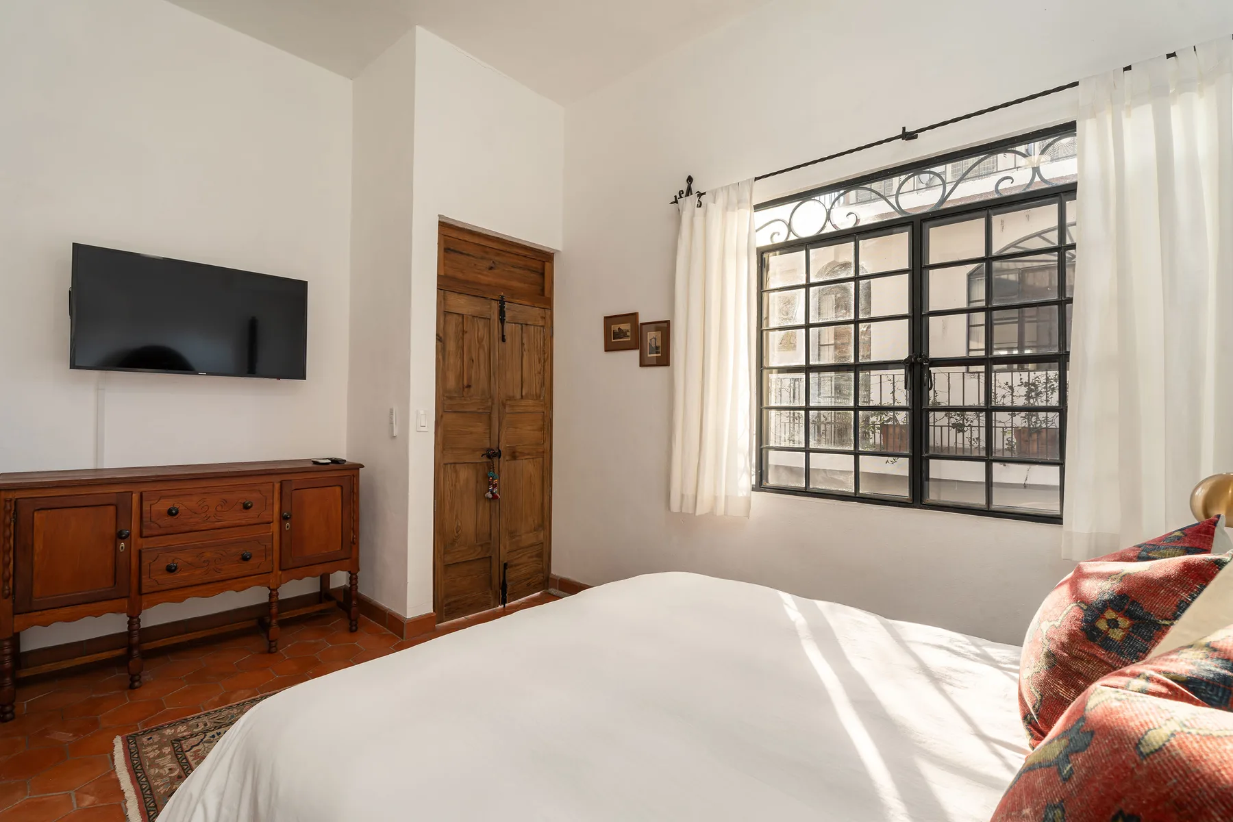 A bedroom with a bed, wooden door, television, and large window.