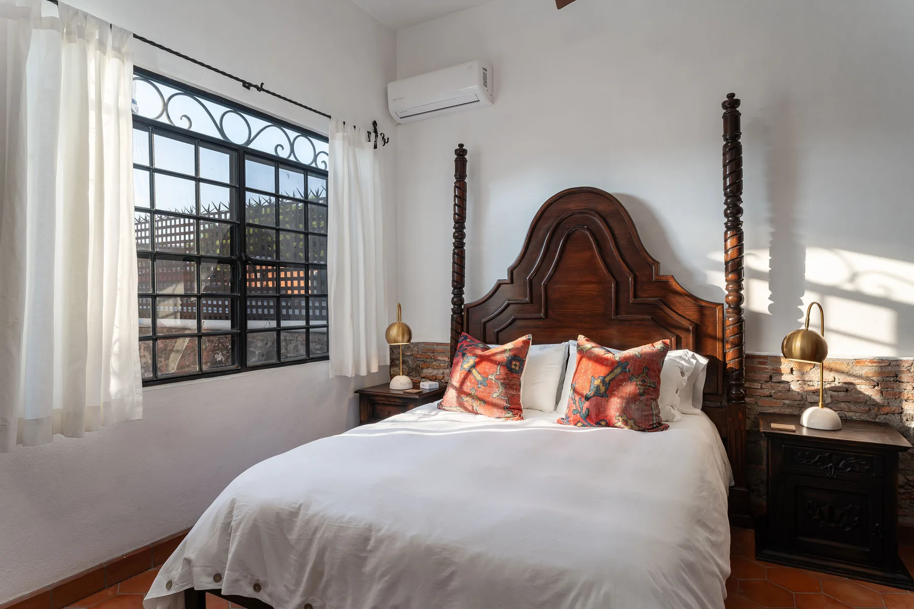 A bedroom with a wooden bed, white bedding, and a large window with curtains.