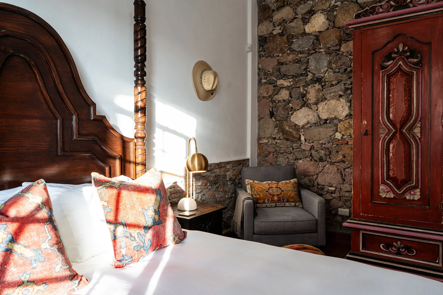 A bedroom with a carved wooden bed, colorful pillows, and a stone accent wall.