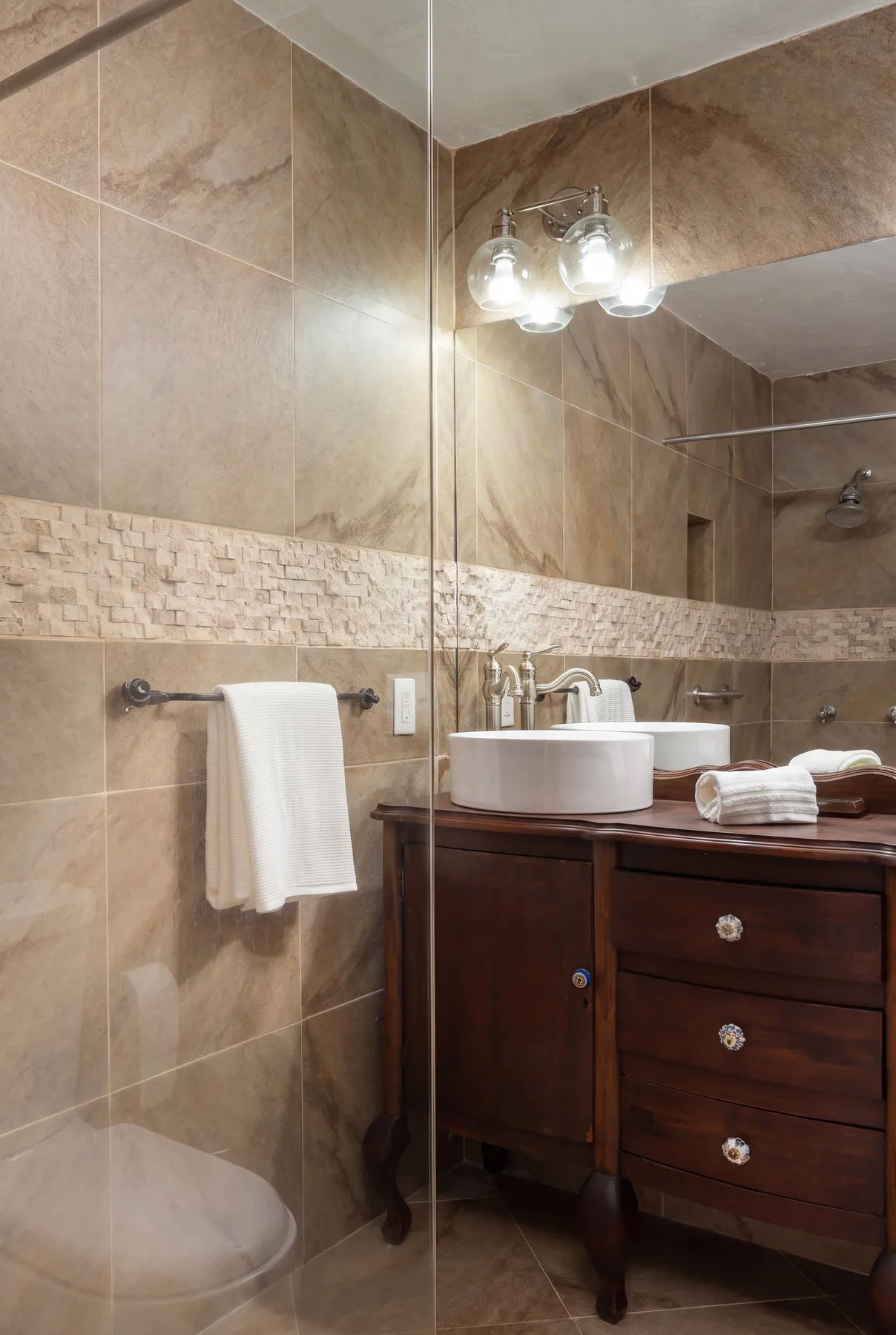 A tiled bathroom vanity with a vessel sink, mirror, and towel.