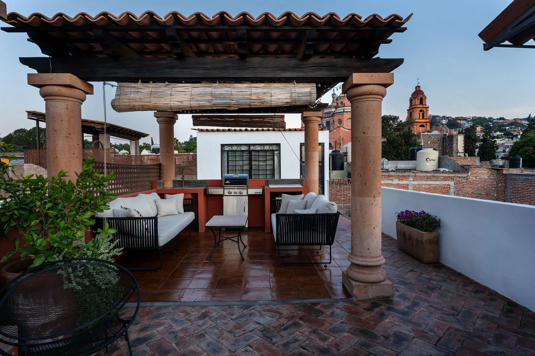 A covered outdoor terrace has seating, a table, and a view of nearby rooftops.