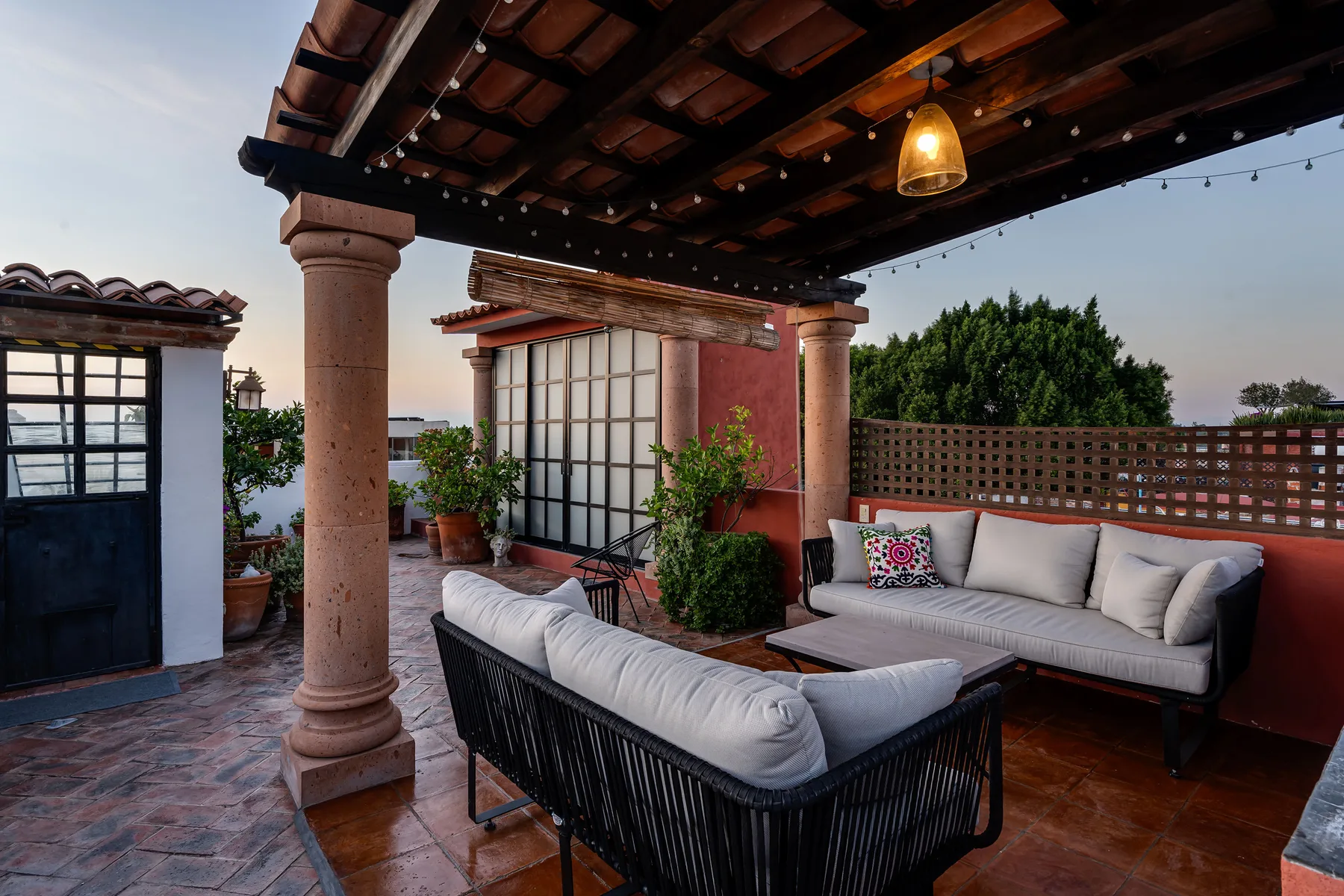Covered outdoor terrace with cushioned seating and potted plants.