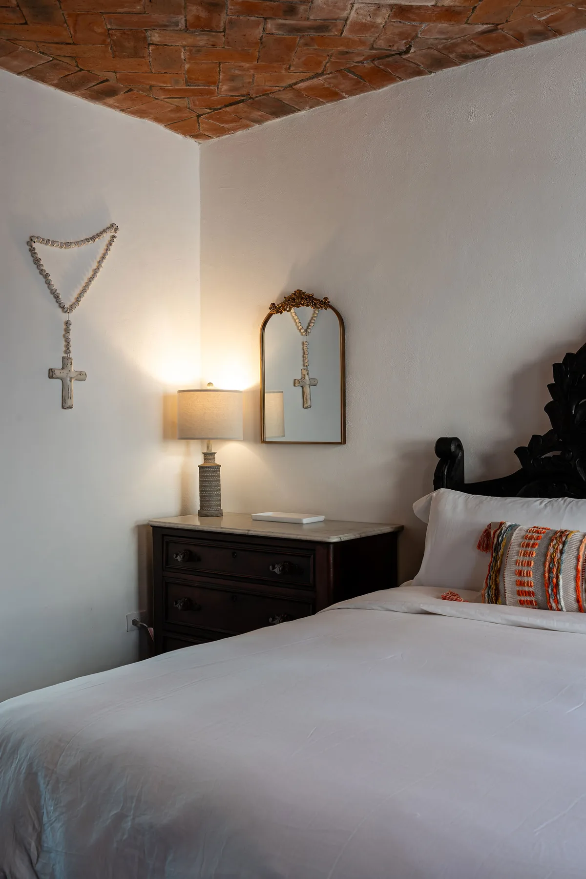 A bedroom with a dark wooden dresser, a mirror, and a neatly made bed.
