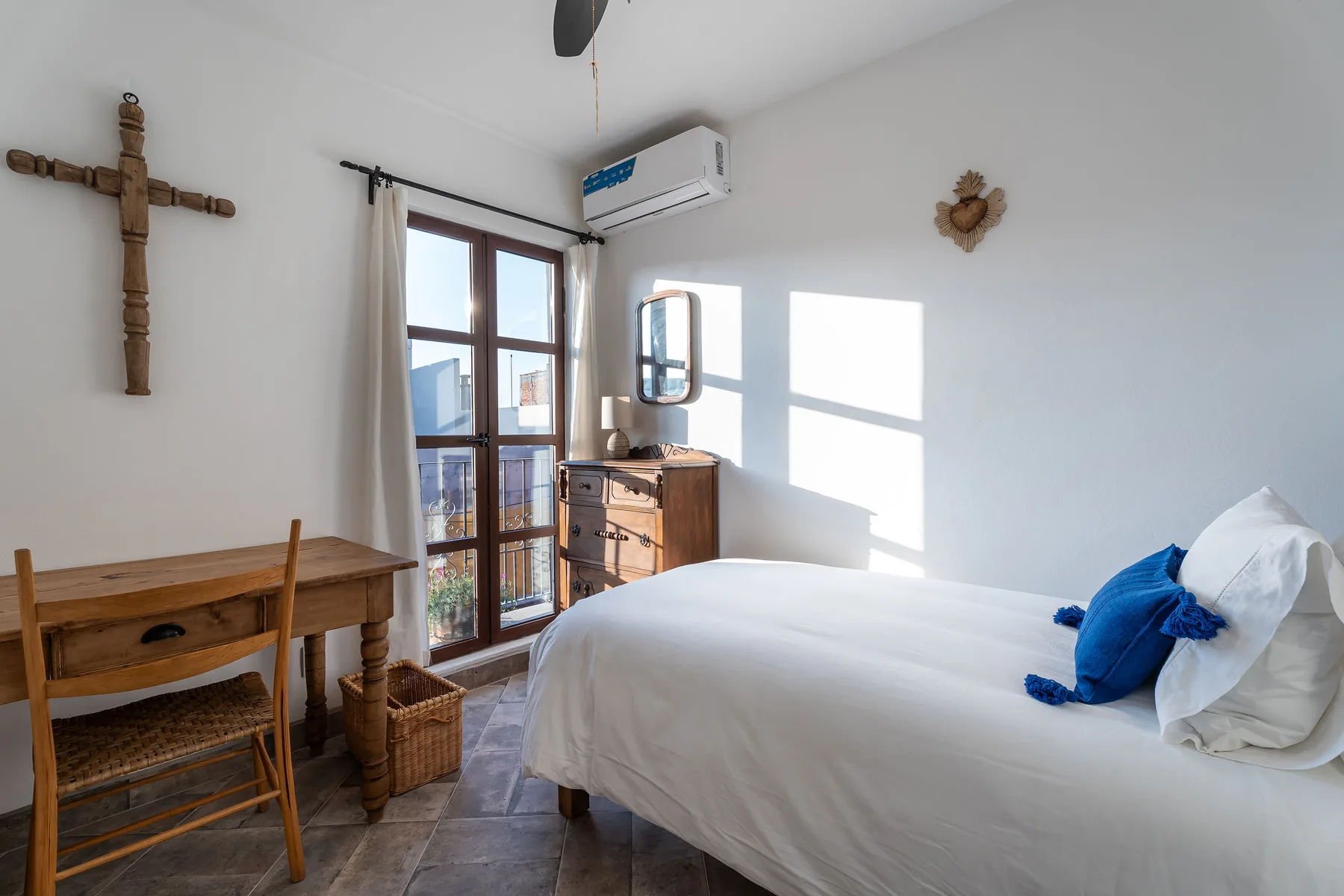 A bright bedroom with a bed, wooden desk, and tall glass doors.