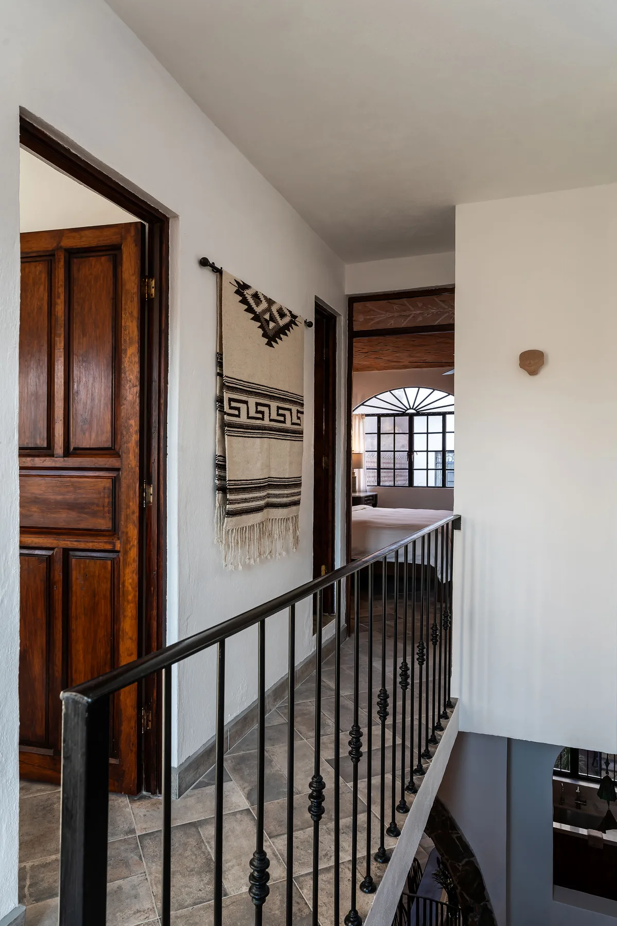 An indoor hallway with a dark metal railing and a woven wall hanging.
