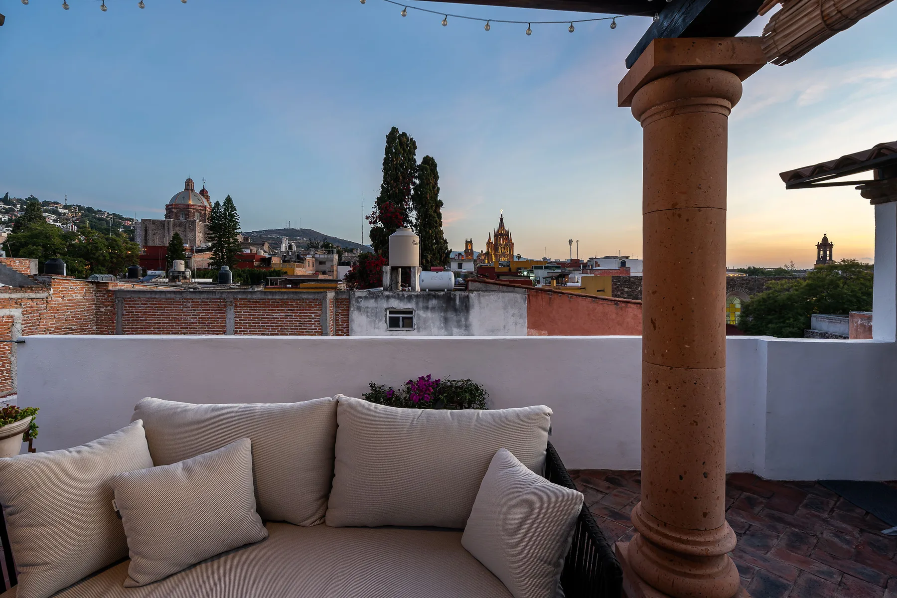A rooftop terrace seating area overlooks nearby rooftops beneath an open sky.