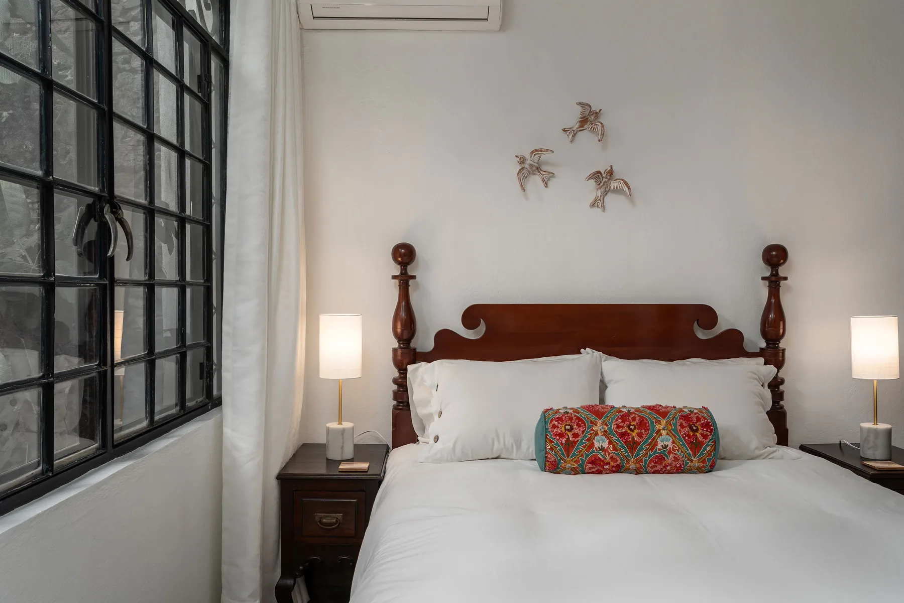 A bedroom with a neatly made bed and a colorful accent cushion.