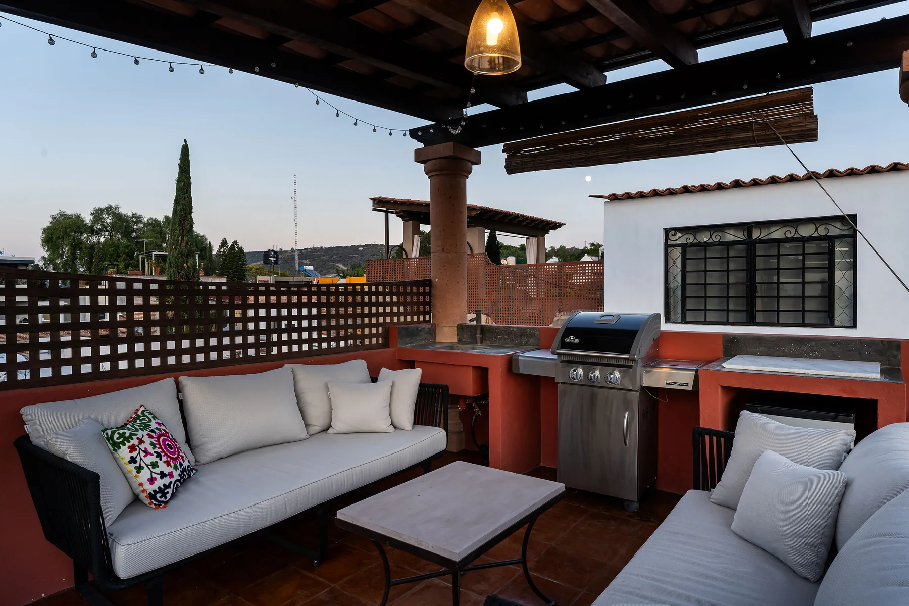 A covered outdoor patio with seating, a dining table, and a built-in grill.