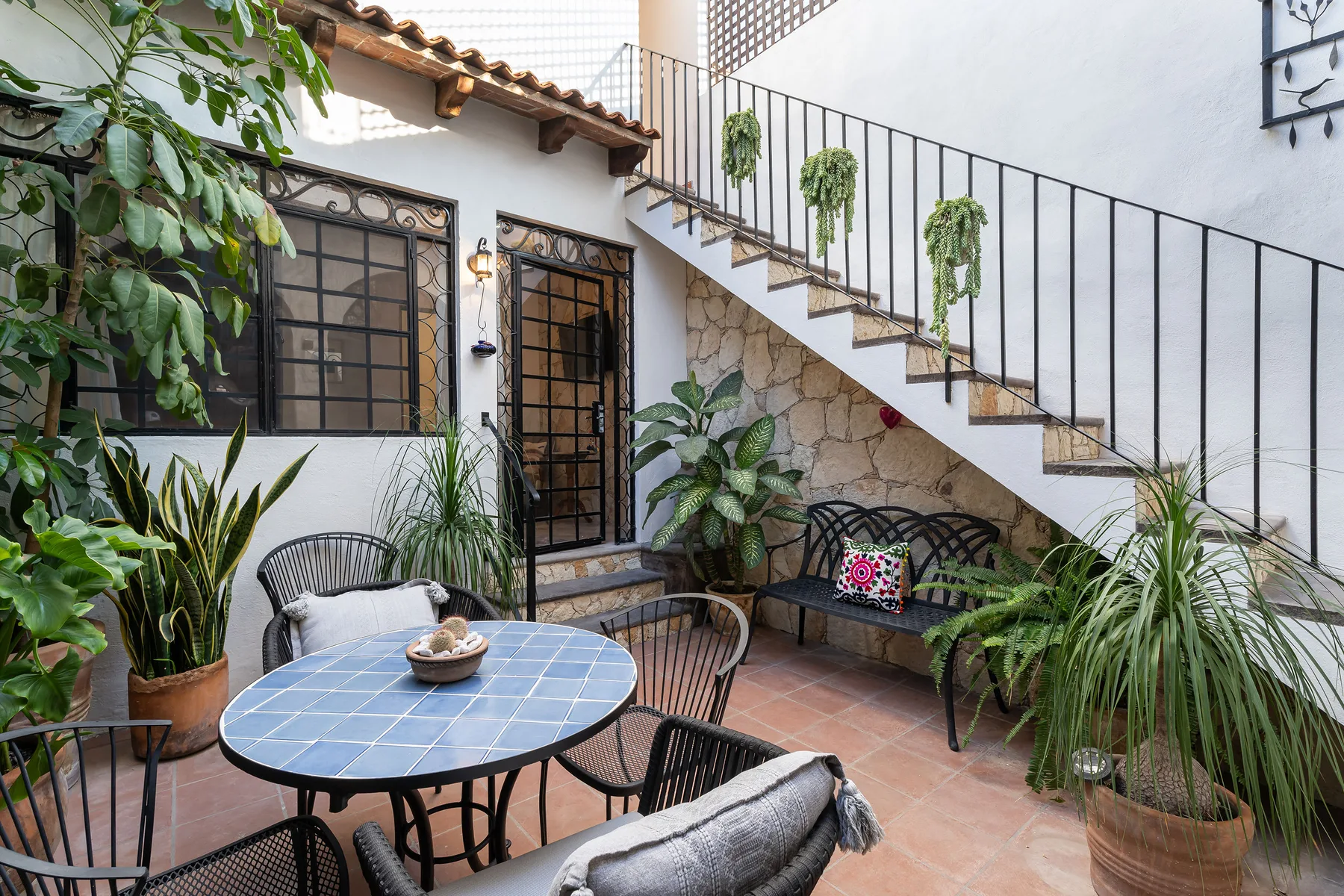 A tiled courtyard patio with a round table, seating, plants, and an outdoor staircase.