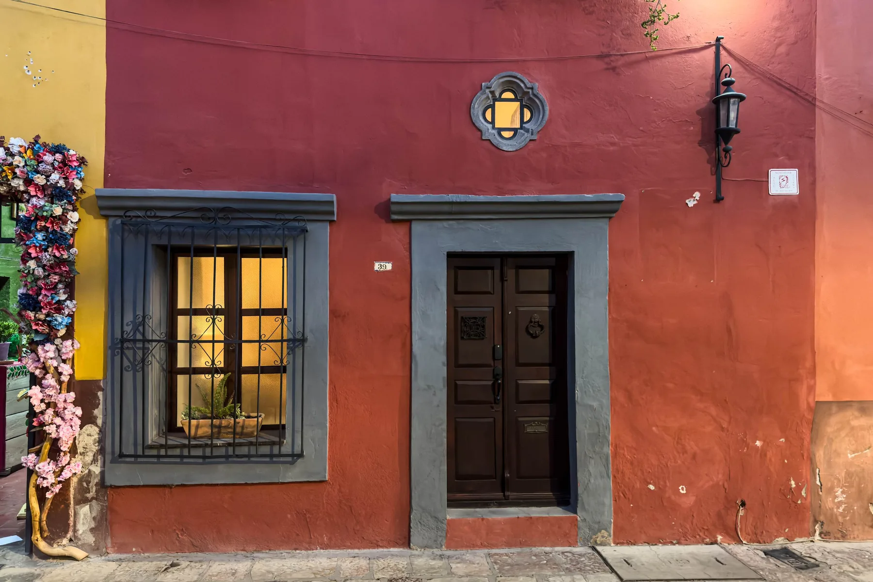 A red stucco building facade with a dark doorway and barred window.