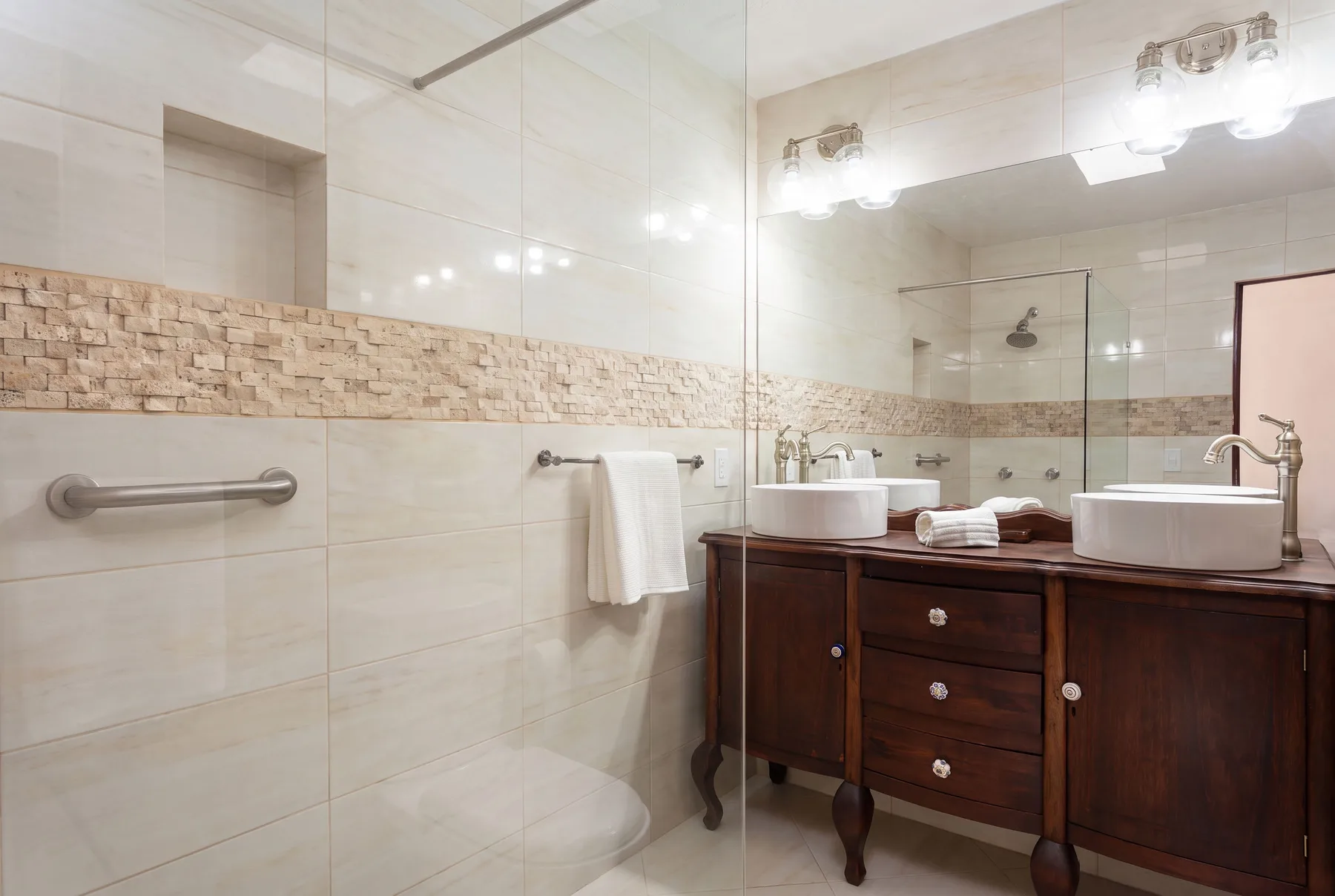 A bright bathroom with a glass shower, double sinks, and a dark wood vanity.