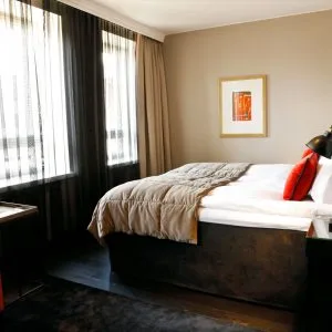 Representative hotel space: A bedroom with a bed beside tall curtained windows.