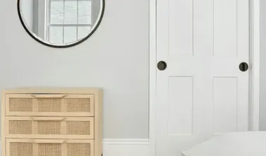 Rincón luminoso de dormitorio con una puerta blanca con paneles y una cómoda de frentes tejidos.