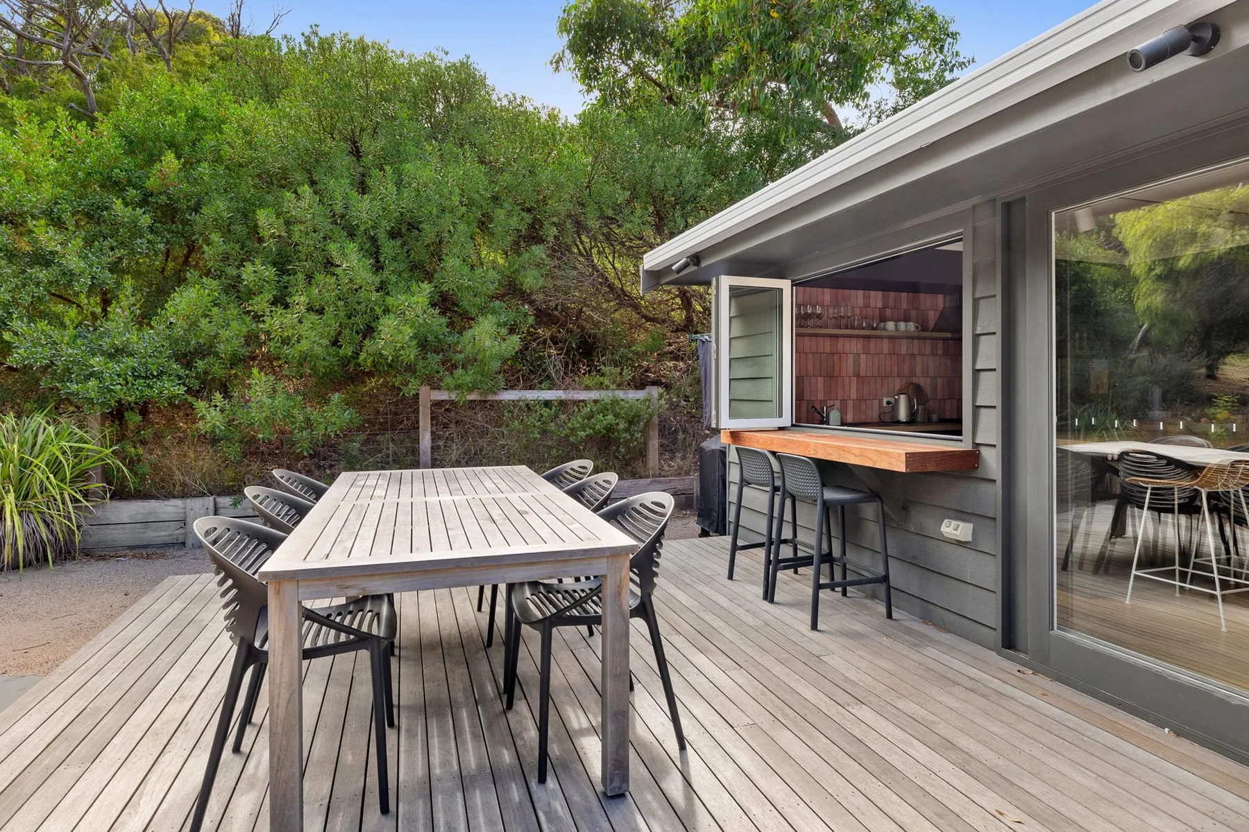 An outdoor dining deck with a long table beside a built-in bar.