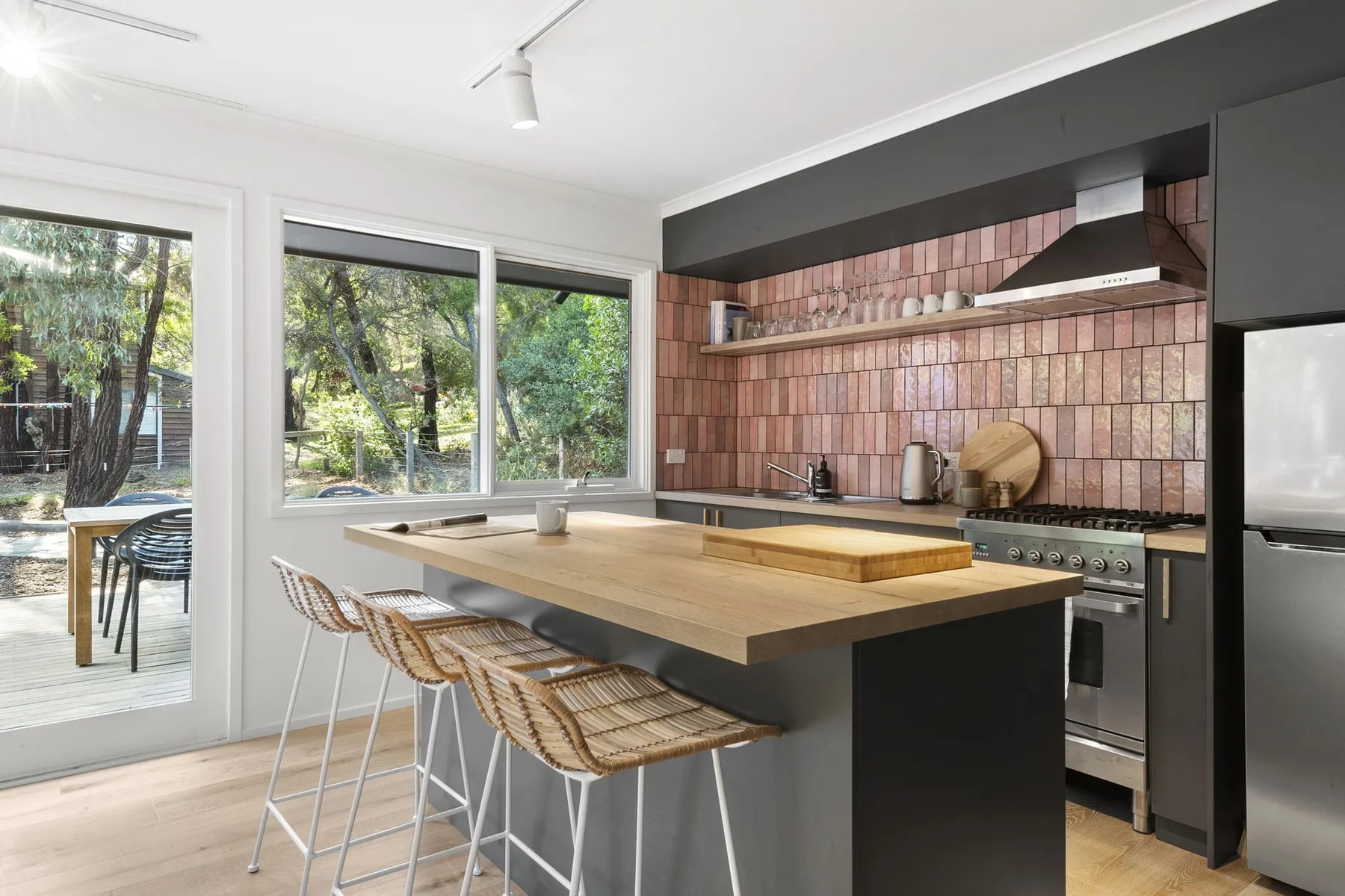 A modern kitchen with a broad island and windows overlooking greenery.