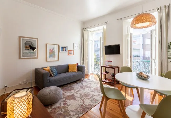 A bright living and dining area with seating, framed artwork, and large windows.