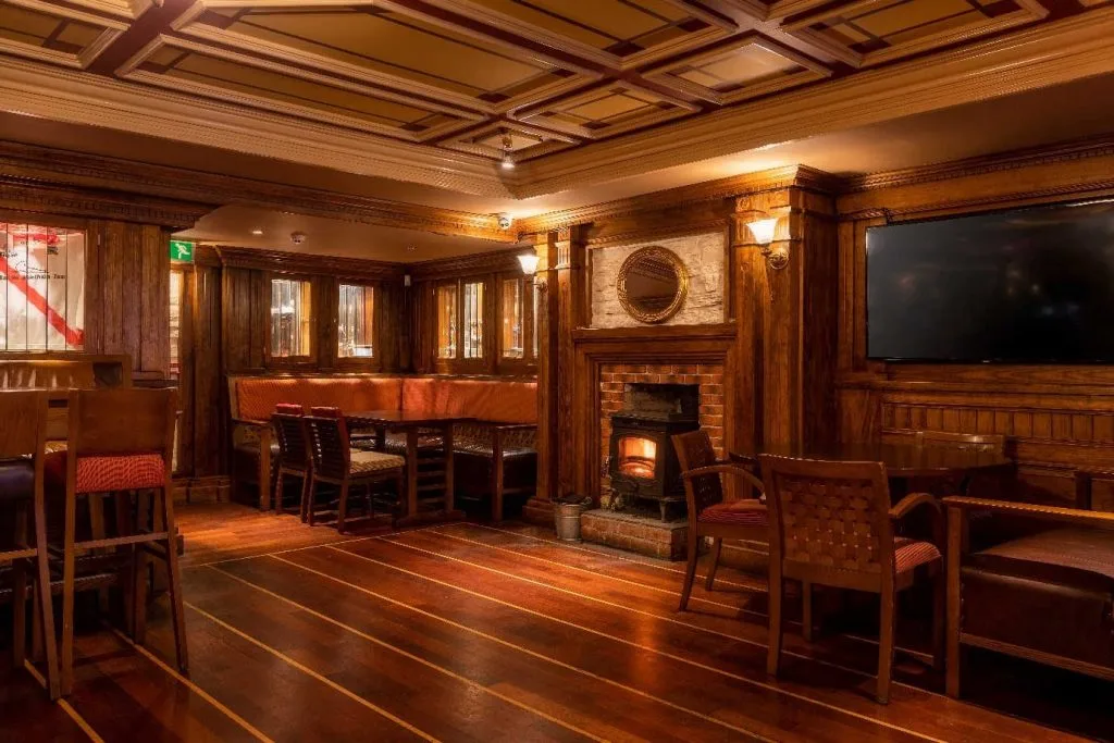 Espacio representativo del hotel: Un salón revestido de madera con mesas, asientos y una chimenea.