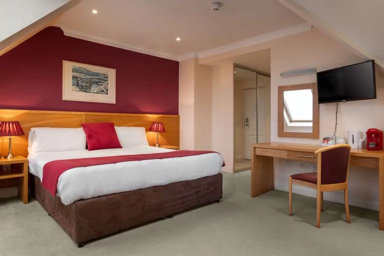 Espacio representativo del hotel: Un dormitorio de hotel con una cama, mesitas de noche y un escritorio bajo un televisor en la pared.