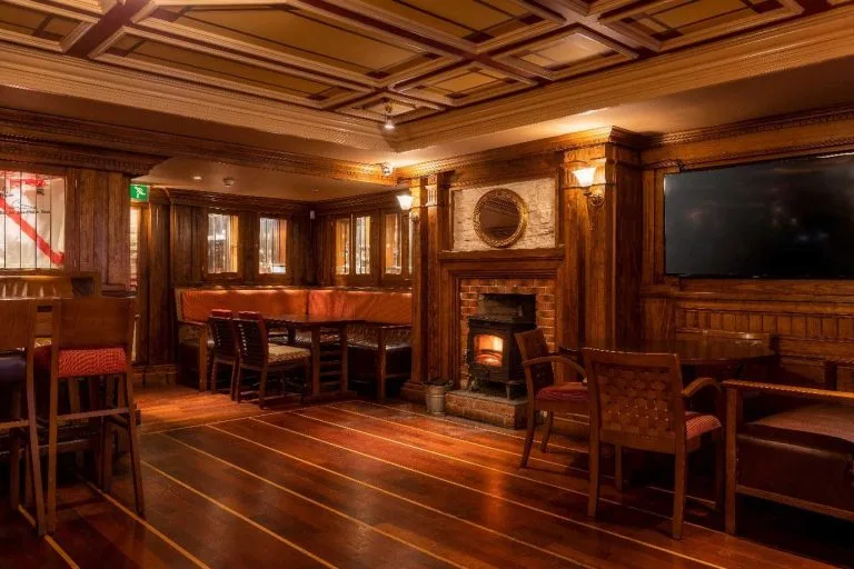 Espacio representativo del hotel: Comedor con paneles de madera, mesas, asientos y una chimenea encendida.