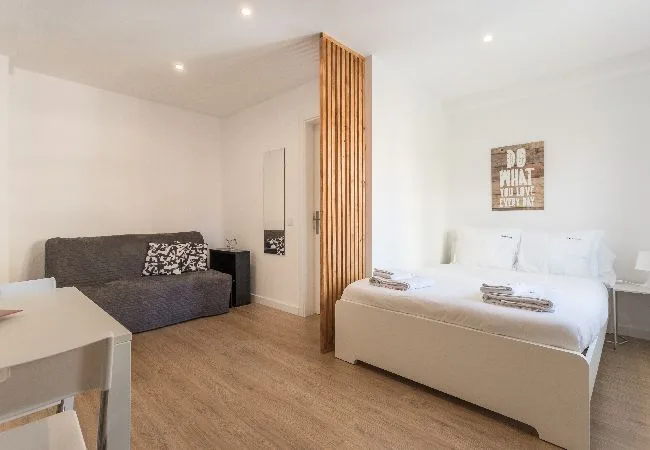A bright bedroom with a bed, a small sofa, and a wooden slatted divider.