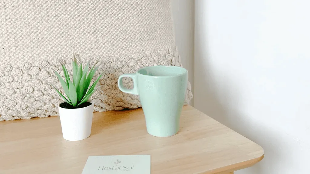 Representative hotel space: A light wood bedside table holds a cup and a small potted plant.