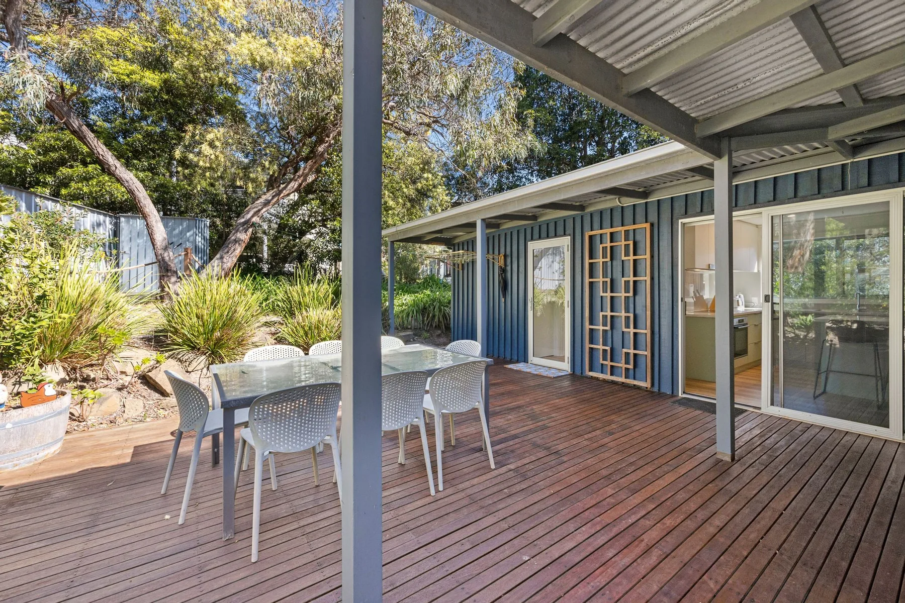 A covered wooden deck with outdoor seating beside a garden.