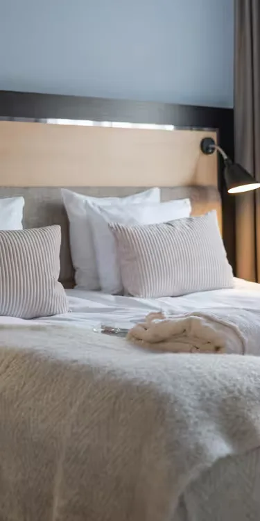 Espacio representativo del hotel: Una cama bien arreglada con almohadas a rayas y una lámpara de lectura junto a la cama.