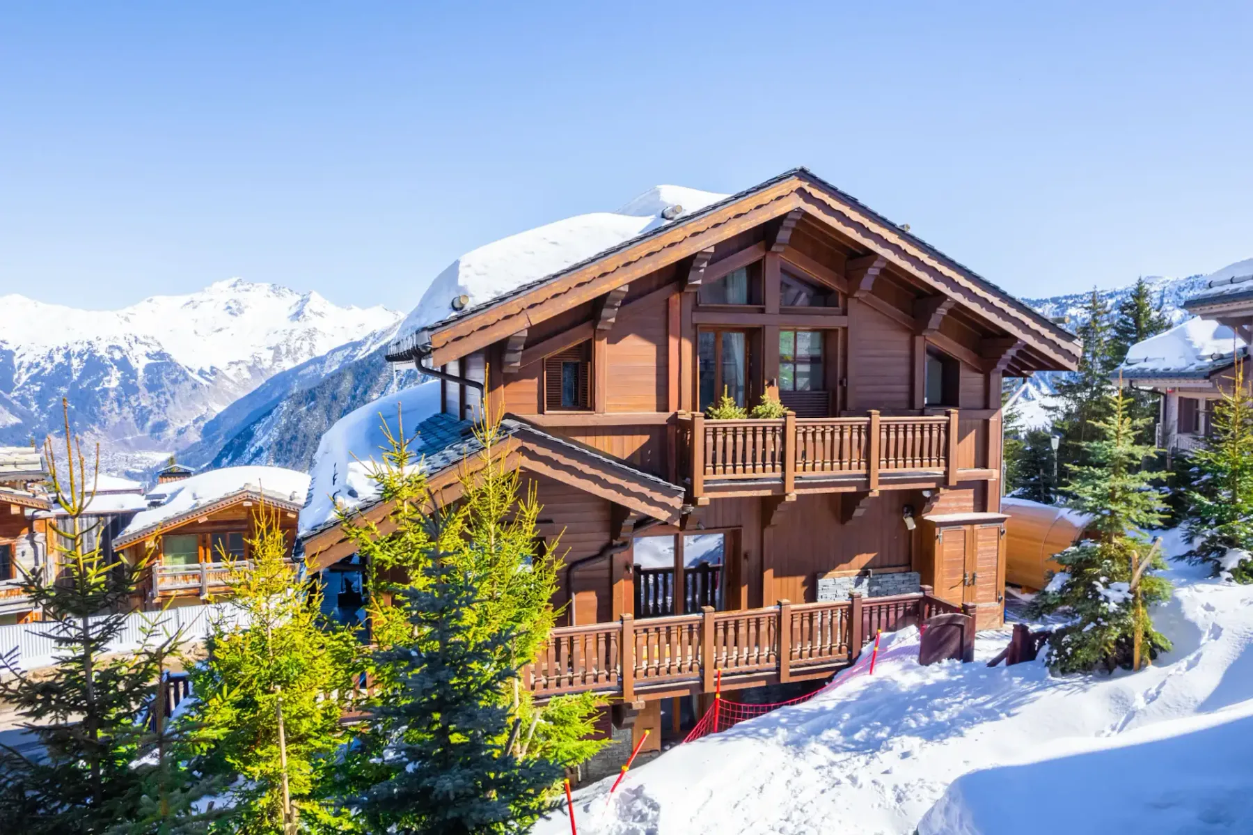 Un chalet de madera se encuentra entre árboles cubiertos de nieve, con montañas nevadas al fondo.