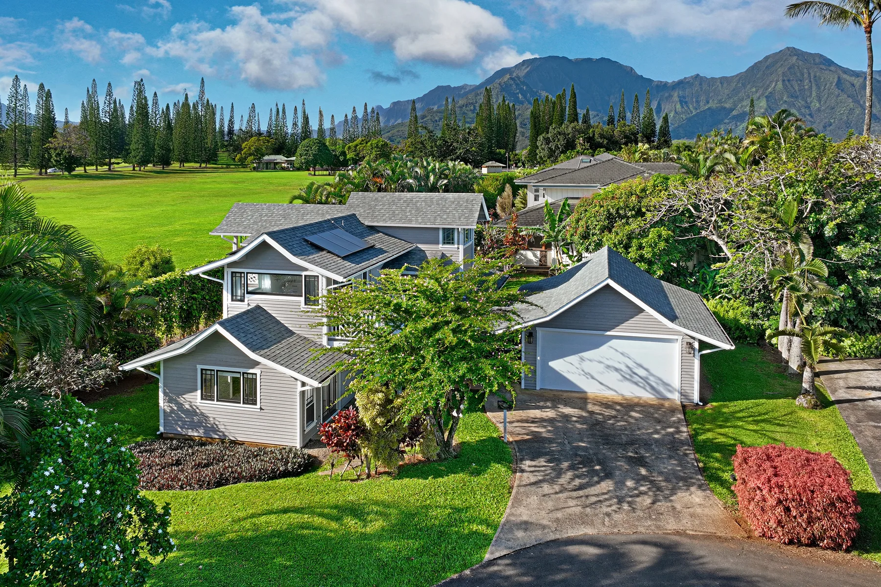 Several houses sit among green lawns and trees, with mountains in the background.