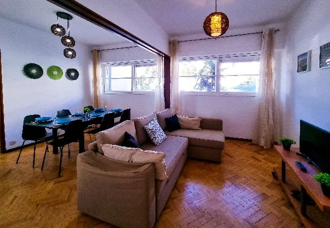 A living room with seating, a dining table, and windows.