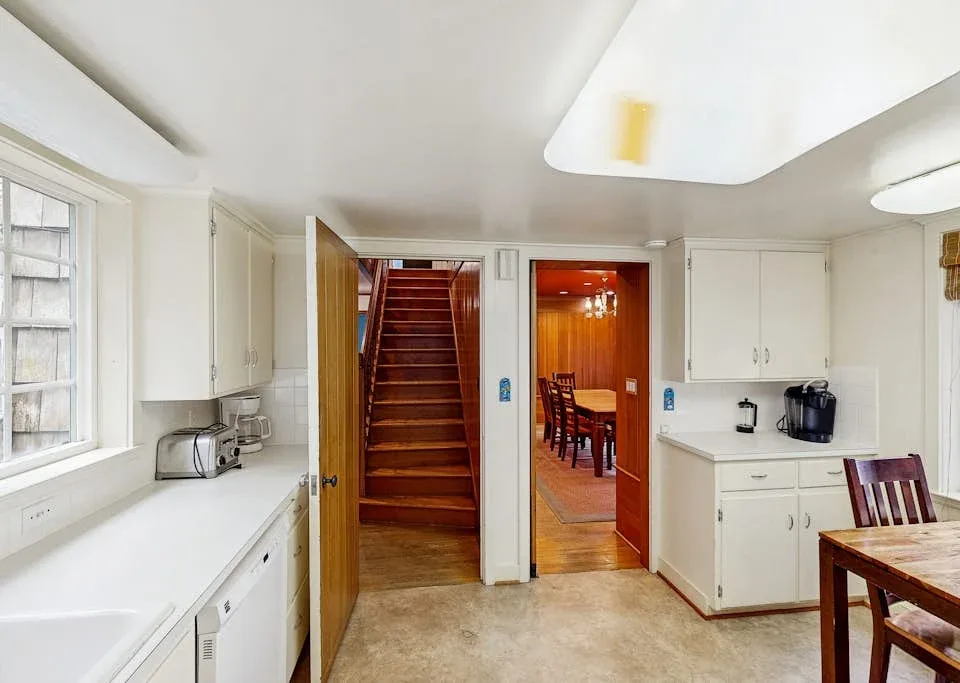 A bright kitchen with white cabinets opens onto a dining area and staircase.