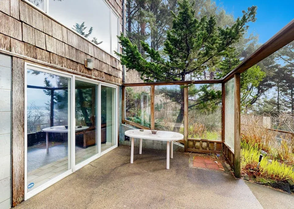 A patio beside large windows overlooks a garden and trees.