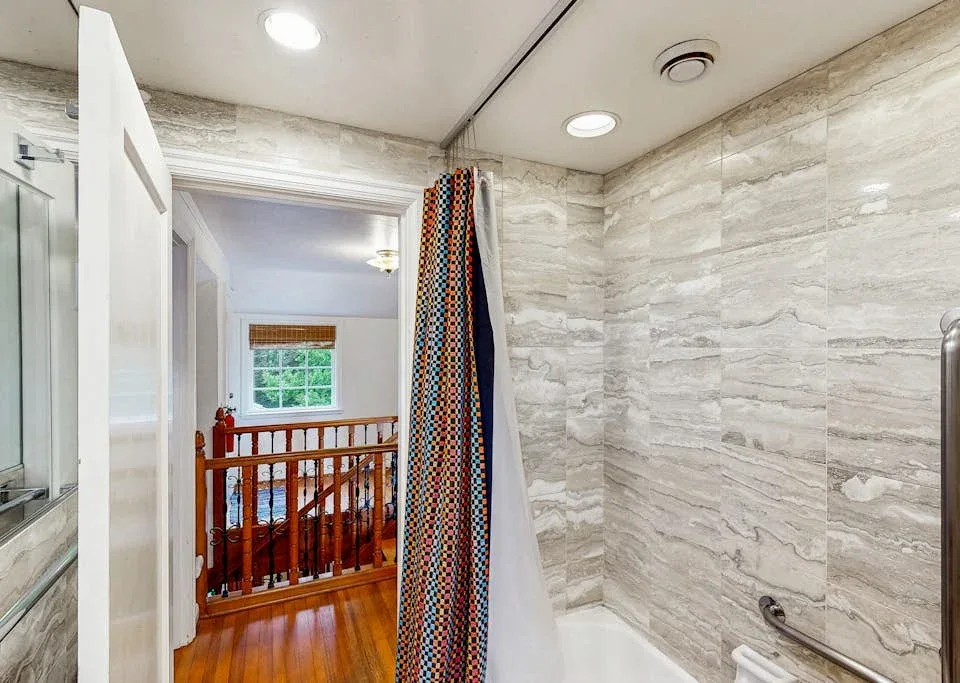 A tiled bathroom with a shower curtain, bathtub, and doorway to a landing.