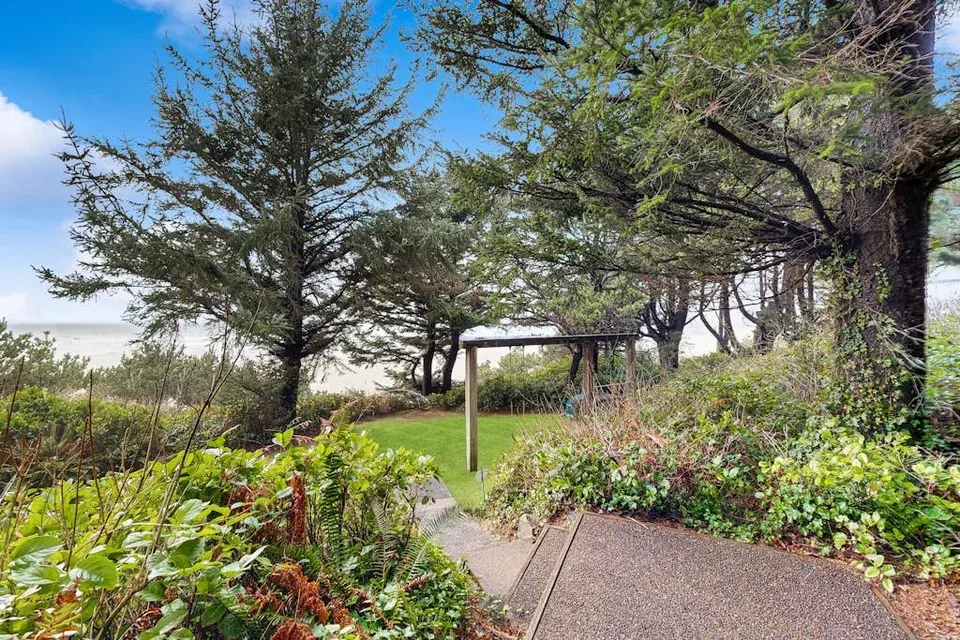 A garden path winds through leafy plantings beneath mature trees.