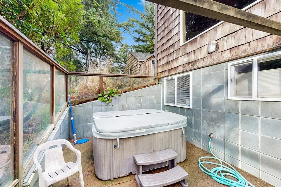 An outdoor hot tub sits in a tiled courtyard beside a privacy fence.