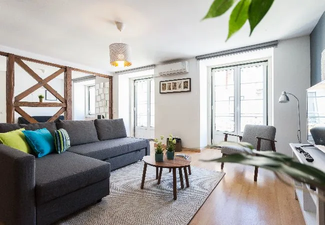 Una sala de estar luminosa con asientos grises, una mesa de centro y ventanas grandes.