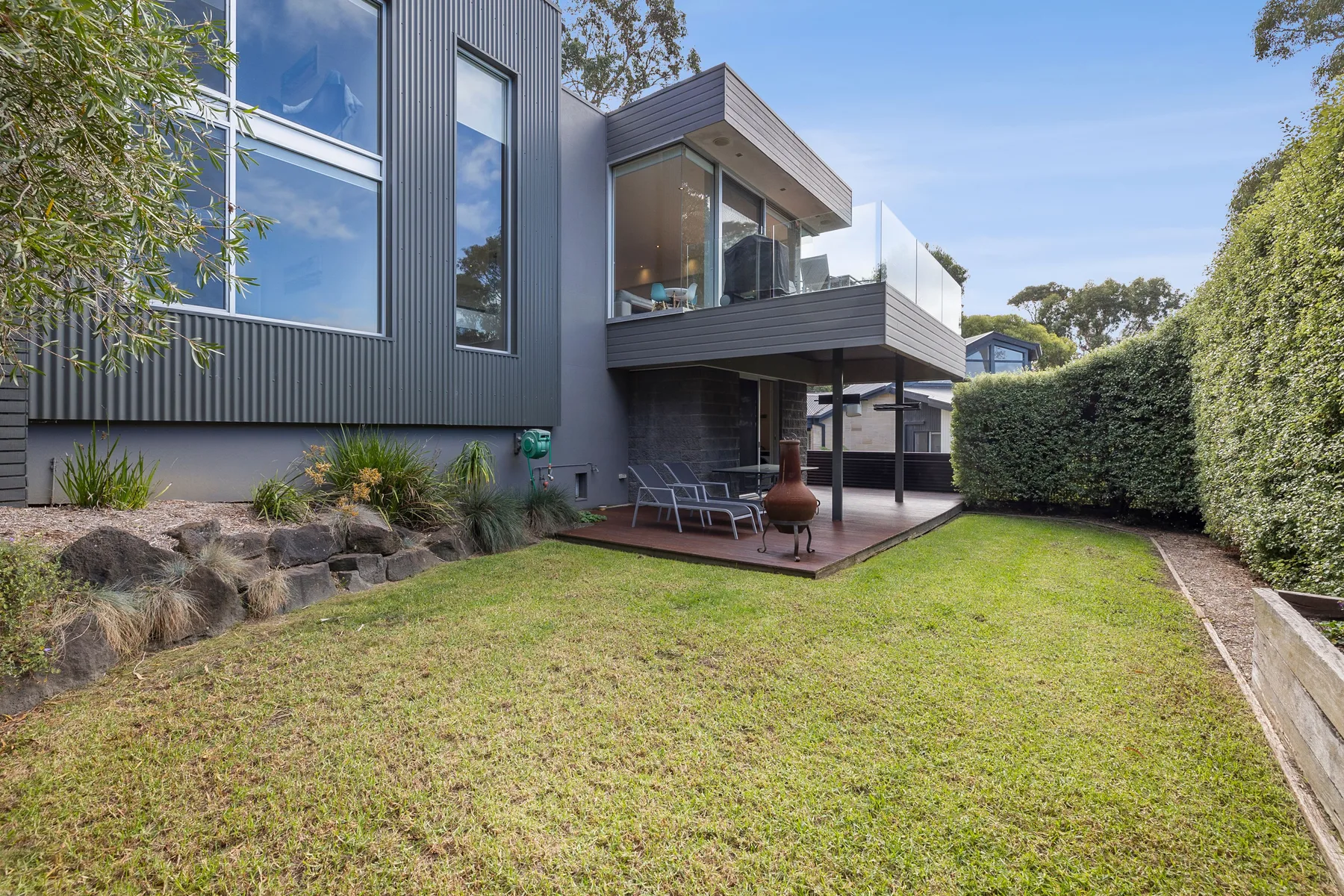 A modern house overlooks a grassy yard with a raised outdoor seating area.