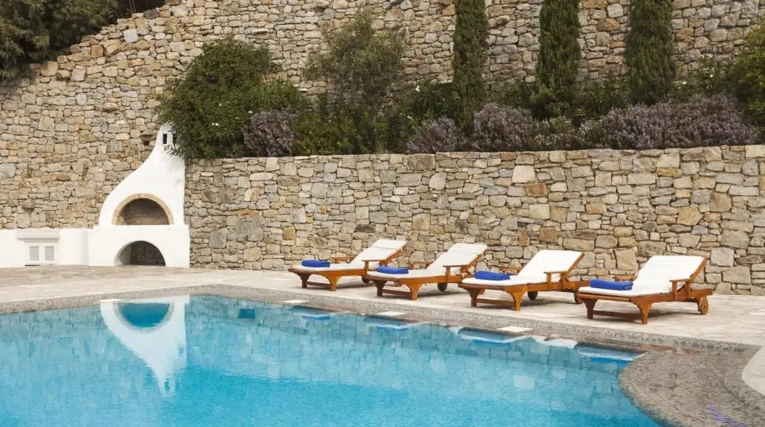 An outdoor swimming pool sits beside a stone wall and a row of loungers.
