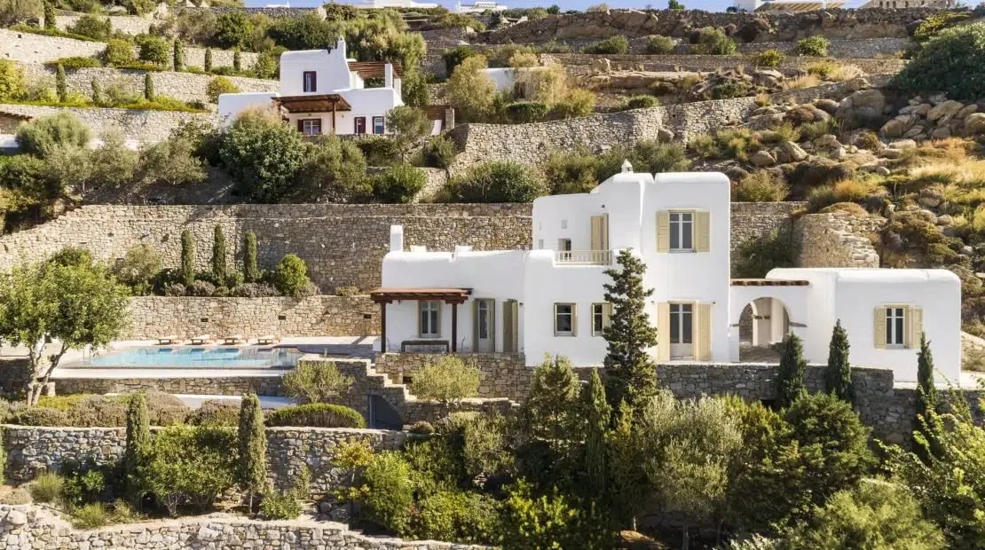 White buildings sit among stone terraces and greenery on a hillside.