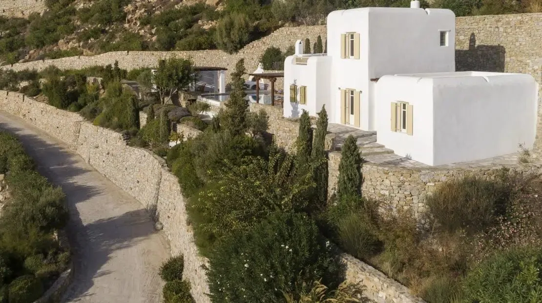 White buildings sit among stone walls and greenery on a hillside.