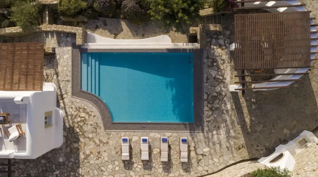 An outdoor swimming pool is surrounded by stone paving and lounge seating.