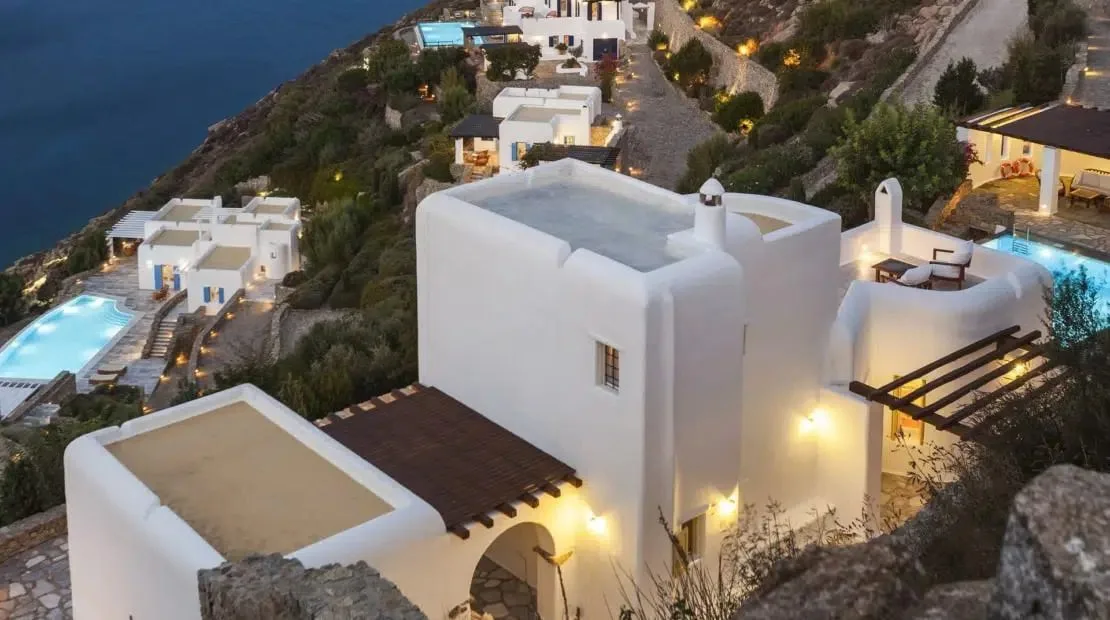 White hillside buildings overlook the sea, with illuminated pools and terraces.