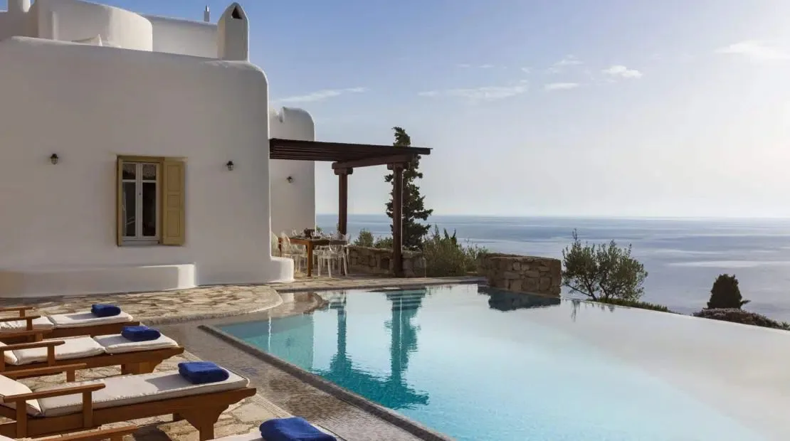 An outdoor swimming pool beside a white building overlooks the sea.