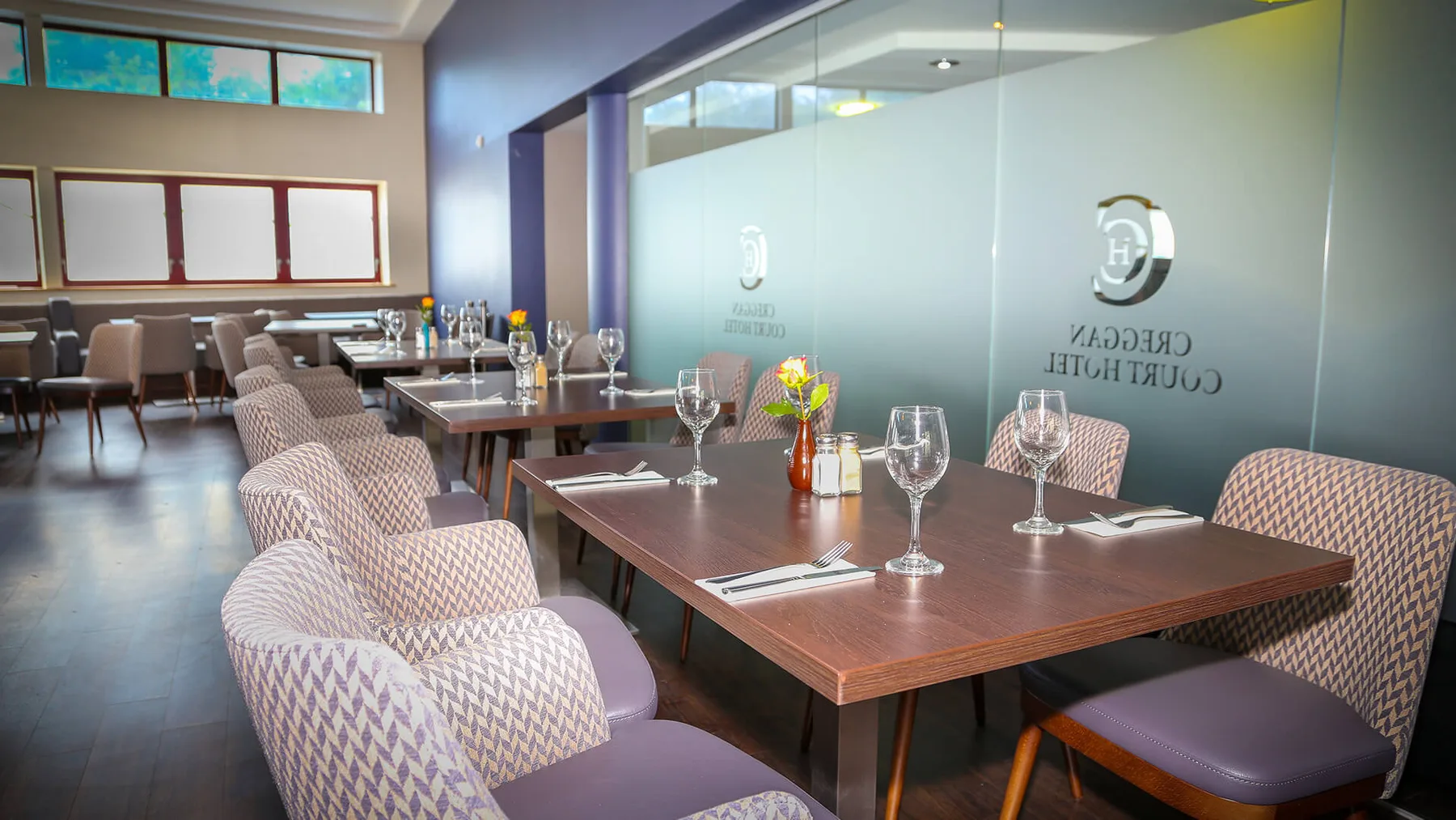 Espacio representativo del hotel: Comedor con mesas y sillas dispuestas junto a un panel de vidrio esmerilado.